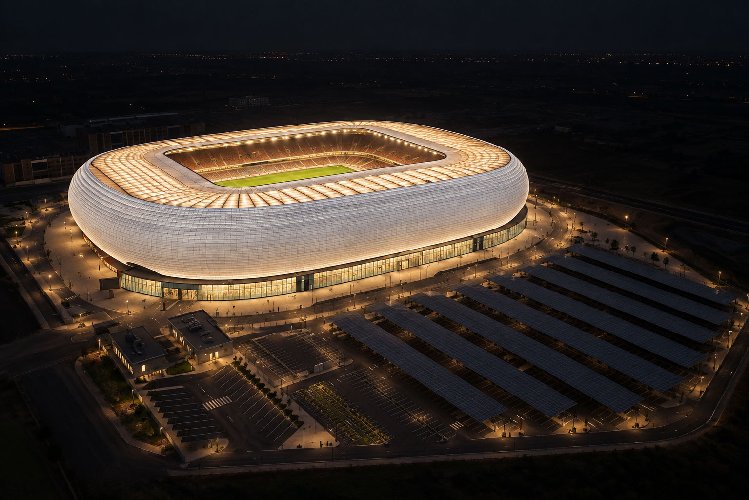 An aerial night view of a large oval stadium with a curved white lattice facade, its interior stands lit, with rows of solar canopies over the car park beside it.