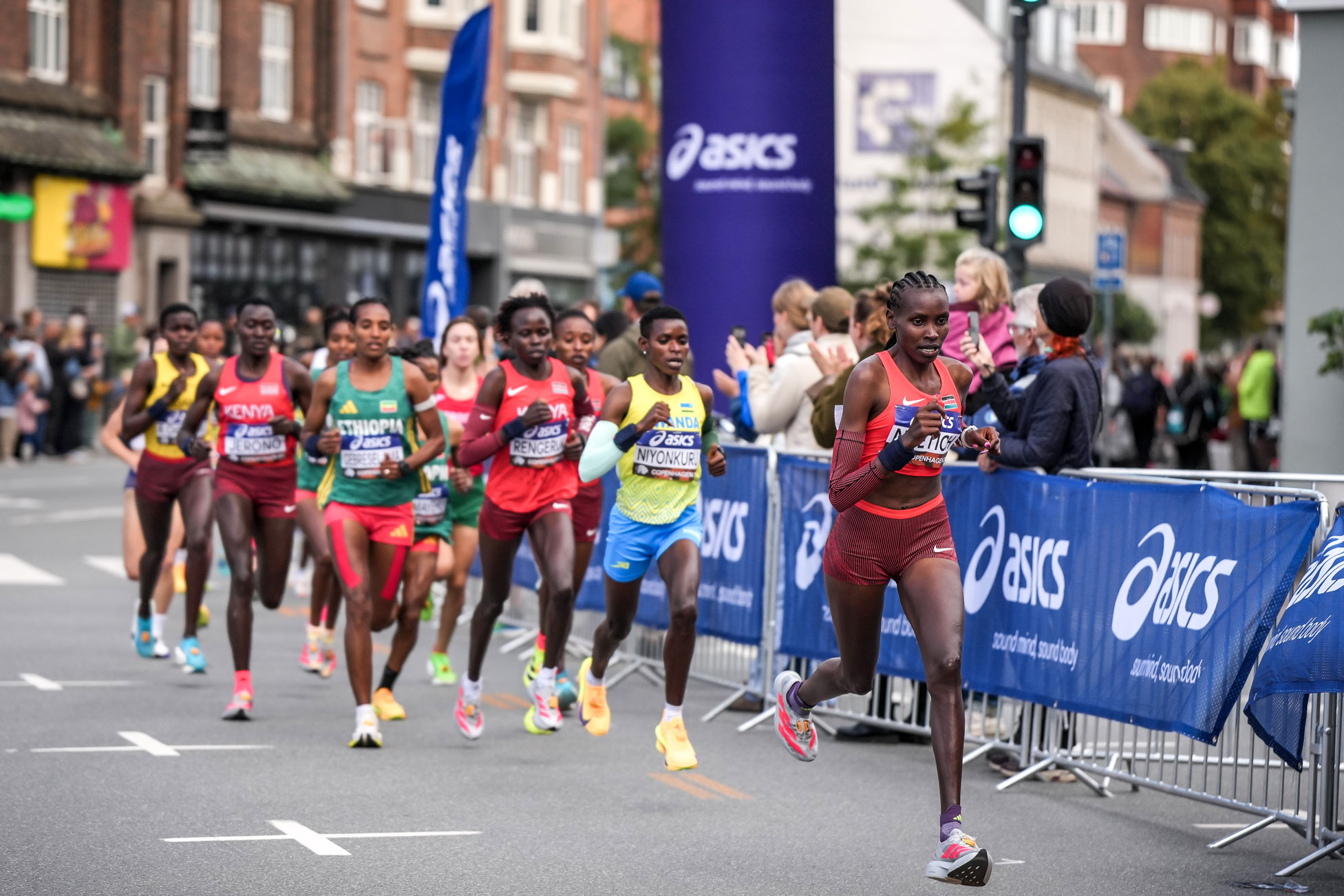 Agnes Jebet Ngetich, in red Kenya kit, running alone at the front of the women's half marathon field on a Copenhagen street, with a chasing pack of runners and spectators behind barriers.